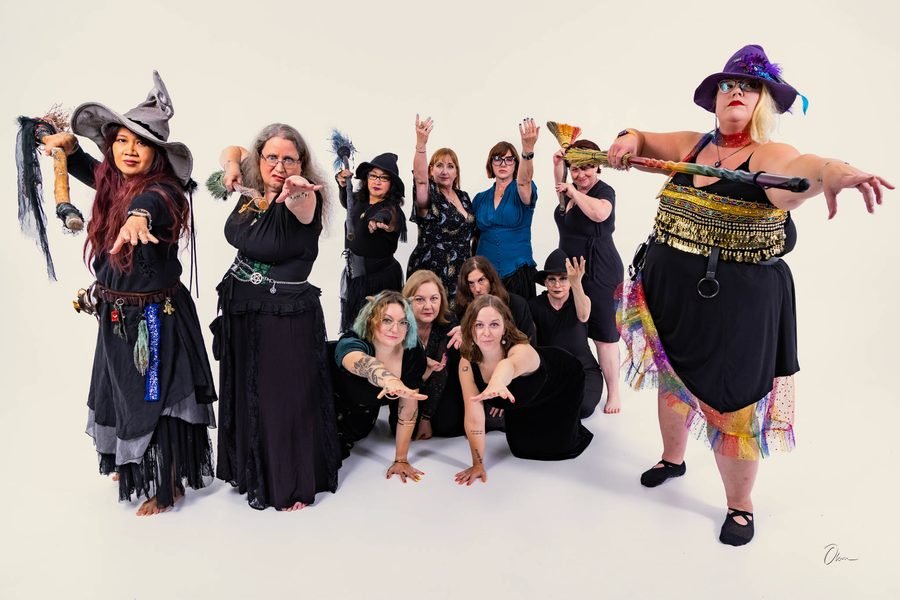 Forest City Dance Circle dancers working through a routine, two dancers in pointed hats holding brooms out to either side while the group reaches forward with outstretched hands.