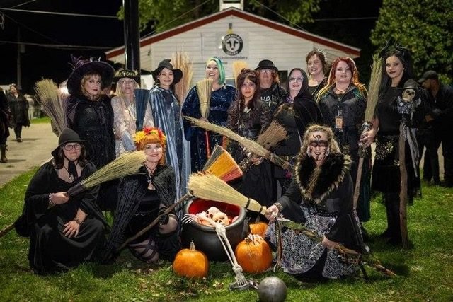Forest City Dance Circle in costume at a past Witch Faire — brooms, a cauldron, and pumpkins under the evening sky in Northern Illinois.